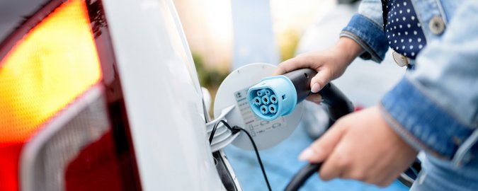 Eine Frau lädt ihr weißes Elektrofahrzeug mit einem schwarzen Kabel mit hellblauem Charging-Point auf.