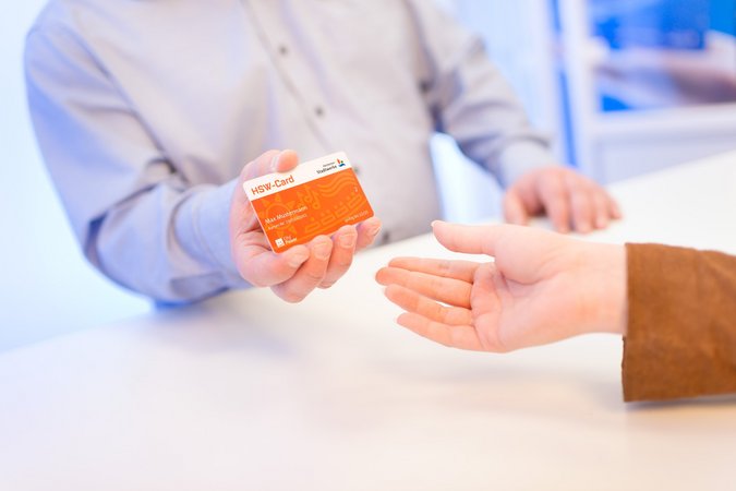 Übergabe einer orangenen Karte im Scheckkartenformat von einer Person auf die andere