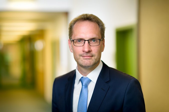 Thorsten Rattmann - Geschäftsführer Stadtwerke Herten Ein blonder Mann mit Brille und blauem Anzug mit hellblauer Krawatte steht vor unscharfem Hintergrund. Er repräsentiert den Geschäftsführer der Stadtwerke Herten.