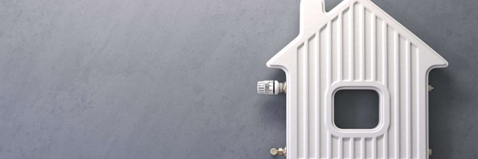 Eine Heizung hängt vor einer grauen Wand. Sie ist in der Form eines Hauses.