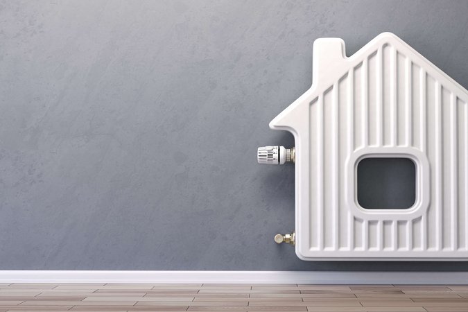 Heizungsanlage erneuern Eine Heizung hängt vor einer grauen Wand. Sie ist in der Form eines Hauses.