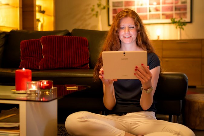 Frau sitzt in ihrem Wohnzimmer und schaut auf ein Tablet