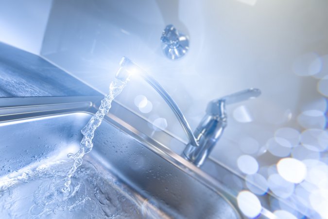 Ein Wasserhahn glänzt in hellem Strahlen während Wasser aus ihm heraus läuft.