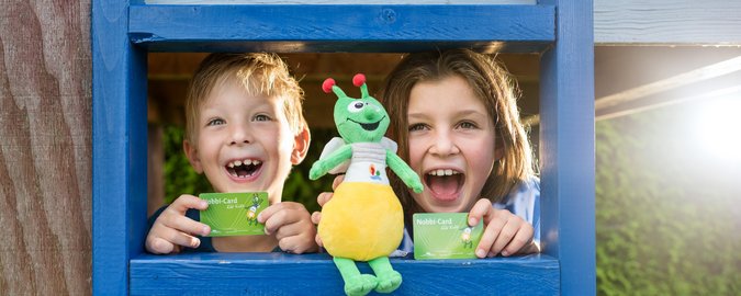 2 Kinder hinter blauer Leiter mit grüner Puppe und grüner Karte im Scheckkartenformat