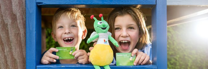 2 Kinder hinter blauer Leiter mit grüner Puppe und grüner Karte im Scheckkartenformat