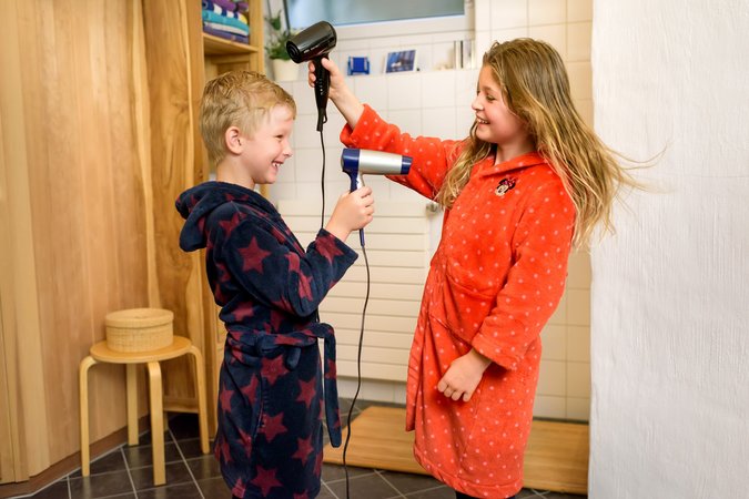 Zwei Kinder im Bademantel mit Föhn in der Hand