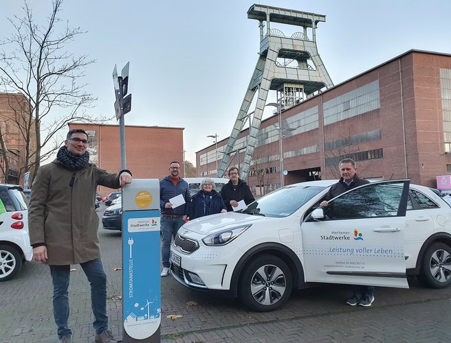 weißer Auto neben blauer Ladesäule mit Menschen