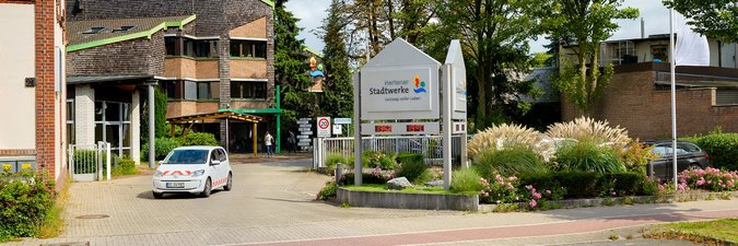 Außenansicht auf ein Gebäude mit Beschilderung "Stadtwerke Herten" und weißem Elektroauto vor der Tür.