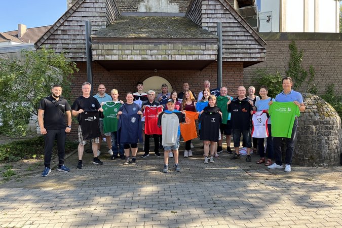 Stadtwerke Herten Trikotsponsoring Gruppe von jungen Erwachsenen vor einem alten Haus, fast jeder der Menschen hält ein Trikot einer anderen Farbe in den Händen