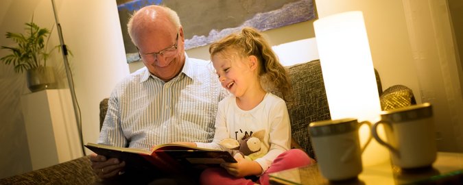Ein Großvater sitzt mit seiner Enkeltochter auf einem Sessel und sie blättern zusammen durch ein Buch.