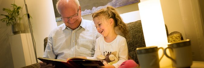 Ein Großvater sitzt mit seiner Enkeltochter auf einem Sessel und sie blättern zusammen durch ein Buch.
