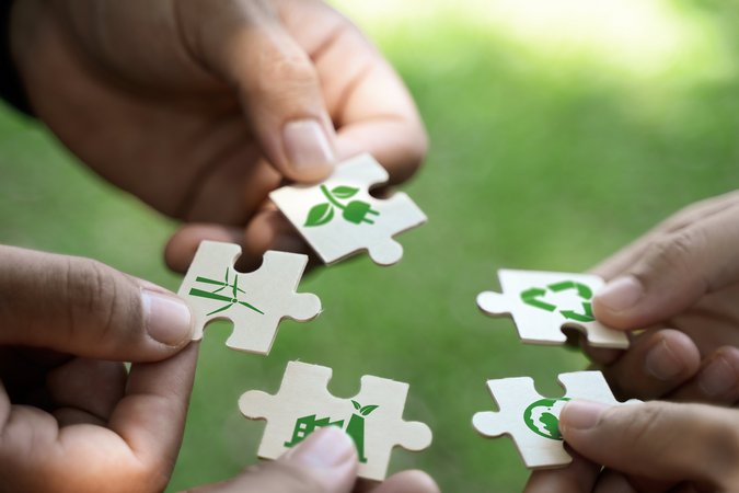 5 Hände die je ein Puzzlestück mit grünen Symbolen halten in der Natur